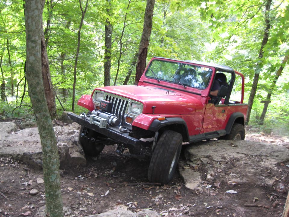 Red Jeep Wrangler navigating rocky terrain off-road. Winch mounted on front bumper