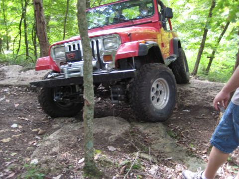 2005 Jeep Wrangler - This red Jeep Wrangler navigates a challenging rocky terrain, its body style suggesting an earlier model year than claimed.