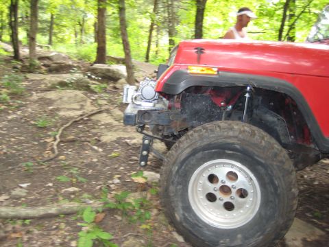 2005 Jeep Wrangler - A red Jeep Wrangler is seen off-road on a rocky trail. The vehicle appears to be from the TJ generation.