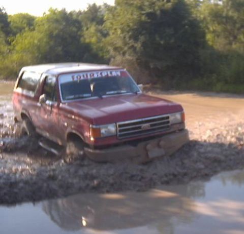 1989 Ford Bronco - Red 1989 Ford Bronco navigates a muddy off-road trail.
