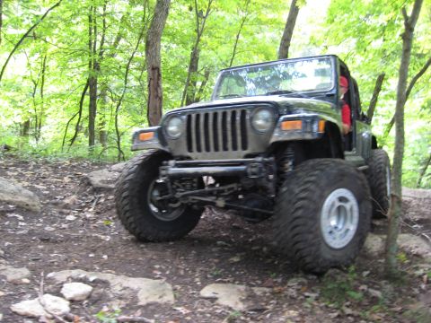 2005 Jeep Wrangler - A black Jeep Wrangler navigates a challenging off-road path through a forest.