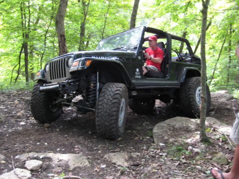 2005 Jeep Wrangler - A black Jeep Wrangler Rubicon navigates a challenging, rocky off-road trail surrounded by trees.