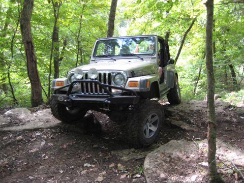 2005 Jeep Wrangler - Silver 2005 Jeep Wrangler driving over rocks on a wooded trail.
