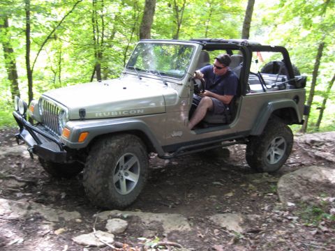2005 Jeep Wrangler - A man drives a tan Jeep Wrangler Rubicon over rocks on a wooded trail.