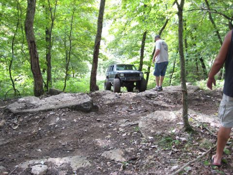 2005 Jeep Wrangler - A modified Jeep Cherokee XJ navigates a challenging rocky trail in a wooded area.
