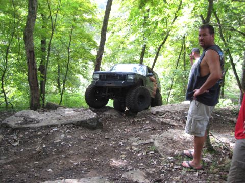 2005 Jeep Wrangler - A heavily modified Jeep Cherokee XJ navigates a rocky off-road course in a wooded area.