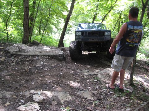 2005 Jeep Wrangler - Modified Jeep Cherokee XJ navigating a rocky, off-road trail in a wooded area.