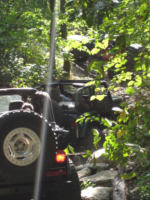 2005 Jeep Wrangler - Two Jeep Wranglers navigate a challenging, rocky off-road trail surrounded by dense foliage.