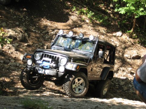 2005 Jeep Wrangler - A black Jeep Wrangler Rubicon navigates a challenging rocky trail with trees in the background.