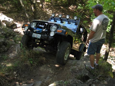 2005 Jeep Wrangler - A black 2005 Jeep Wrangler tackles a challenging rocky path, with a man observing the off-road action.