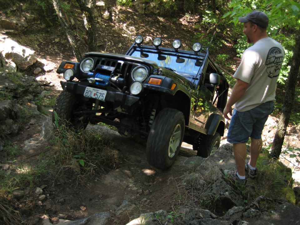 Black 2005 Jeep Wrangler navigating a rocky trail with a man standing nearby