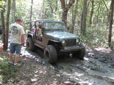 2005 Jeep Wrangler - Jeep Wrangler off-roading through mud and trees. Another vehicle is seen in the background.