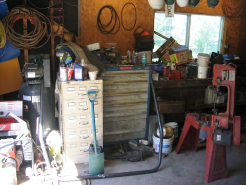 1986 Ford Bronco - A cluttered garage scene contains various tools, storage units, and a red band saw.