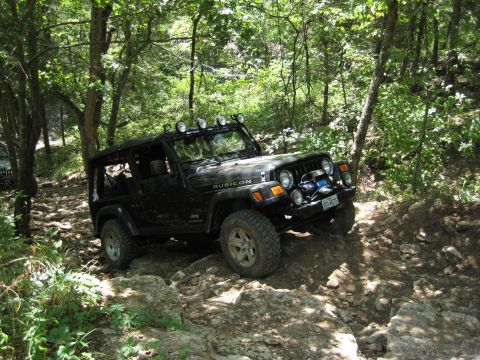2005 Jeep Wrangler - A black Jeep Wrangler Rubicon navigates a challenging rocky path through a forest.