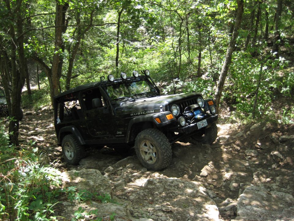 Black Jeep Wrangler Rubicon driving on a rocky, wooded trail