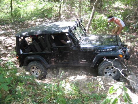 2005 Jeep Wrangler - A black 2005 Jeep Wrangler Rubicon is shown navigating a challenging rocky trail with a person standing on the hood.