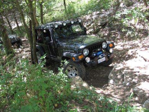 2005 Jeep Wrangler - Two Jeeps off-roading on a wooded, rocky trail. The lead Jeep is a Rubicon model.