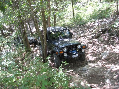2005 Jeep Wrangler - Two Jeep Wranglers navigate a challenging, rocky path through a dense forest.