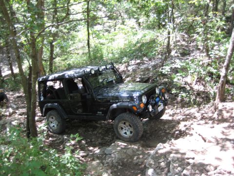 2005 Jeep Wrangler - A black Jeep Wrangler Rubicon navigates a rocky off-road trail surrounded by trees.