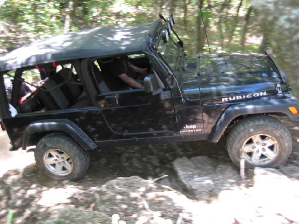 Black Jeep Wrangler Rubicon driving over rocks on a trail. It's a 2005 model
