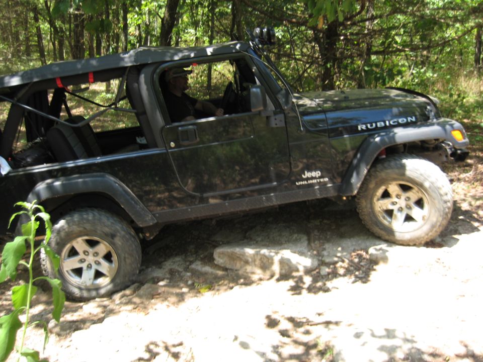 Black Jeep Wrangler Rubicon Unlimited on rocky terrain, driver visible, soft top up