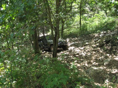 2005 Jeep Wrangler - A green Jeep Wrangler navigates a challenging rocky trail through a wooded area.