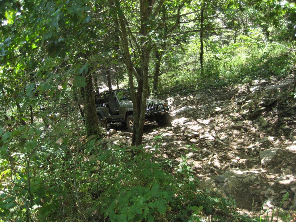 Green Jeep Wrangler on a rocky trail, 3/4 front view
