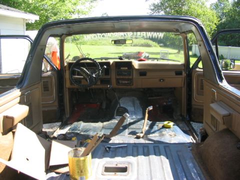 1986 Ford Bronco - The interior of a 1986 Ford Bronco is shown with its doors open, revealing a disassembled cabin and evidence of a roll cage installation.