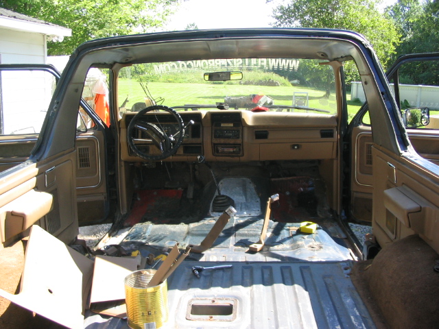 Rear-to-front interior view of gutted tan Ford Bronco with bare metal floor