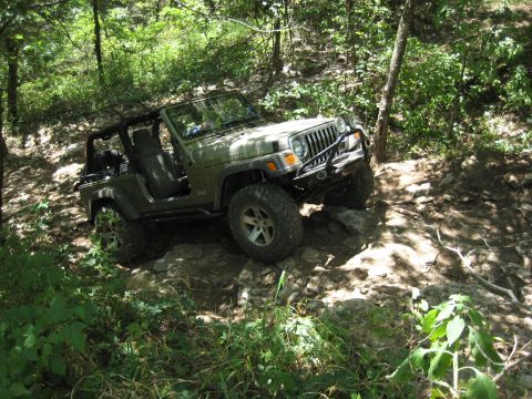 2005 Jeep Wrangler - Elevated view of a khaki long-wheelbase Jeep Wrangler Unlimited, topless and doorless with the bare roll cage exposed, crawling over a rock…
