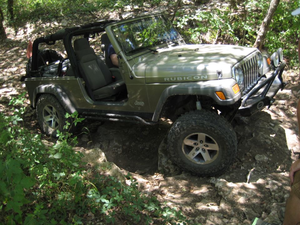 Green 2005 Jeep Wrangler Rubicon driving over rocks on a trail