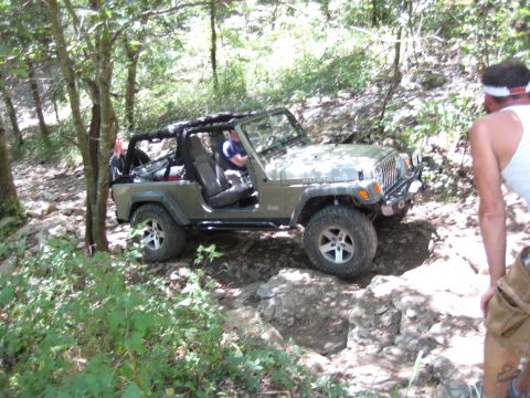 2005 Jeep Wrangler - A Jeep Wrangler navigates a rocky path through a wooded area, with a person watching from the side.