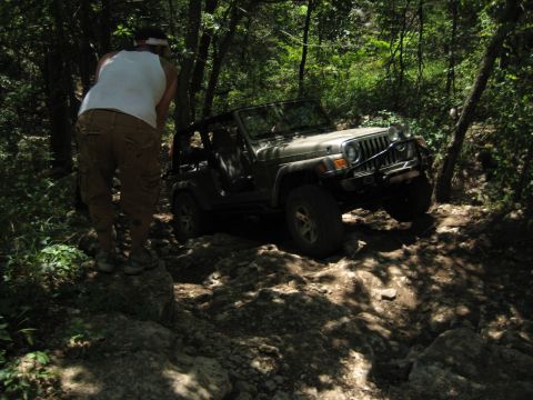 2005 Jeep Wrangler - A person watches a tan Jeep Wrangler traverse a challenging, rocky off-road path.