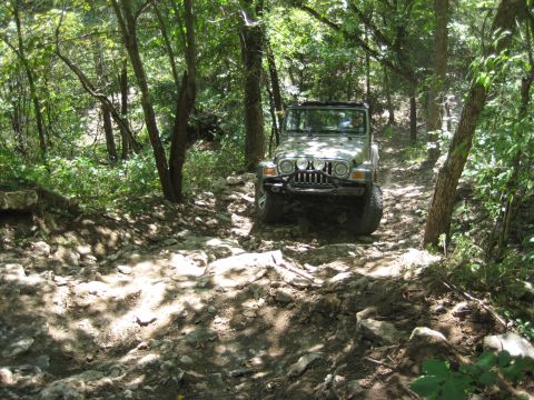 2005 Jeep Wrangler - A Jeep Wrangler navigates a challenging, rocky path through a dense forest.