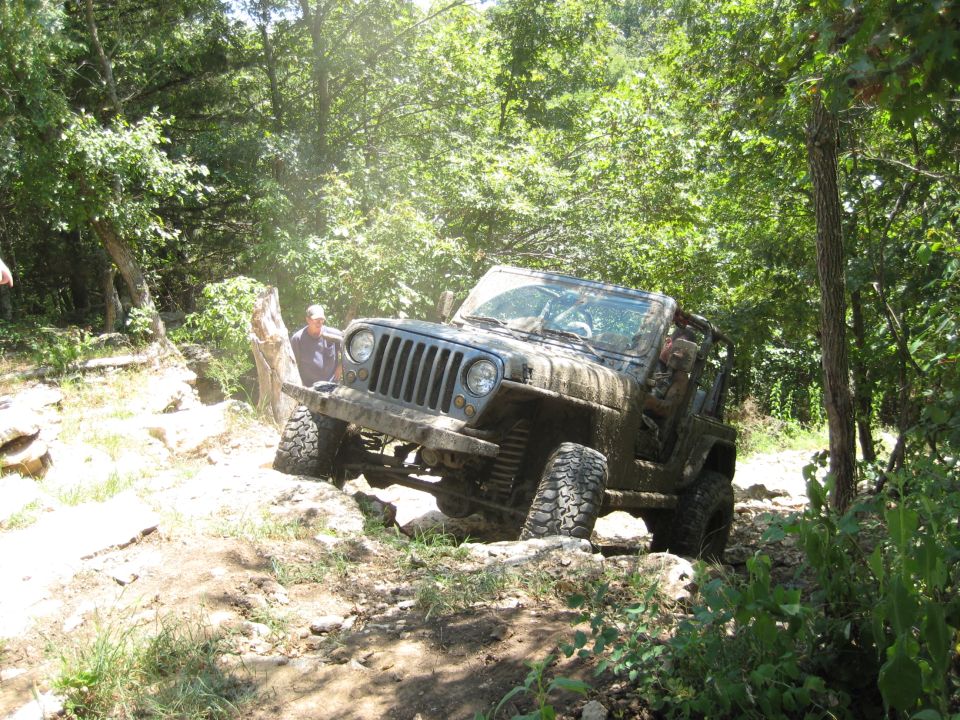 Muddy 2005 Jeep Wrangler navigating a rocky, wooded trail