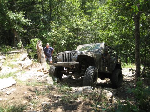 2005 Jeep Wrangler - A man watches a Jeep Wrangler navigate a challenging off-road course through a wooded area.