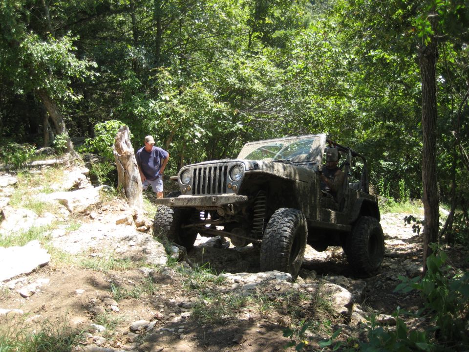 Muddy Jeep Wrangler on rocky trail with a man standing nearby