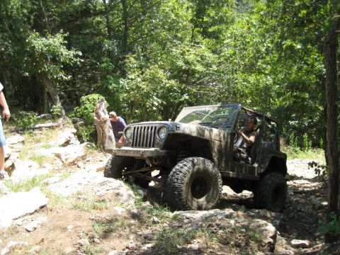 2005 Jeep Wrangler - A 2005 Jeep Wrangler navigates a challenging off-road course with dense foliage surrounding the path.