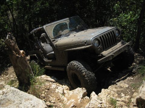 2005 Jeep Wrangler - A mud-splattered Jeep Wrangler navigates a challenging rocky trail.