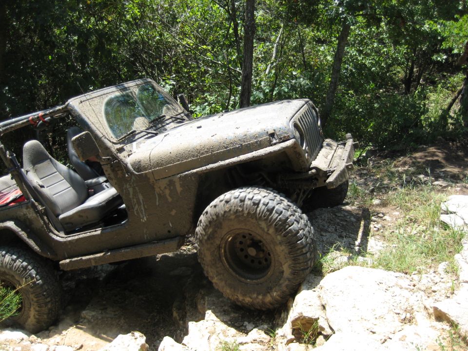 Muddy Jeep Wrangler navigating rocky terrain on a trail