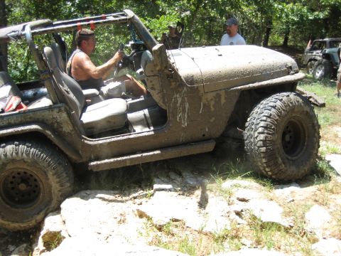 2005 Jeep Wrangler - A mud-splattered 2005 Jeep Wrangler navigates a rocky trail with a driver at the wheel.