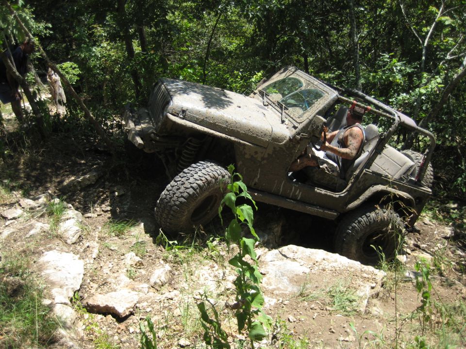 Mud-covered 2005 Jeep Wrangler navigating a rocky, wooded trail