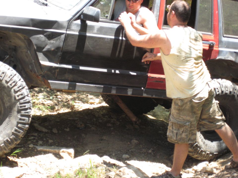 Man in white shirt helps driver in black Jeep Cherokee XJ stuck on trail