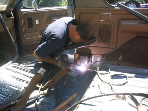 1986 Ford Bronco - Man welding inside the interior of an older SUV, with tools and a spare tire visible.