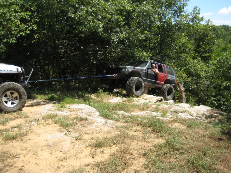 Black Jeep Cherokee XJ with red rear doors being towed by a white Jeep Rubicon on a rocky trail
