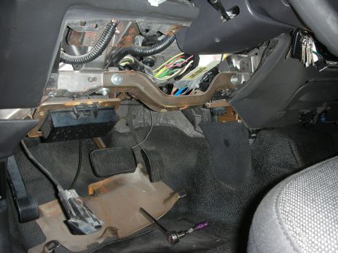 2004 Ford Crown Victoria - The interior of a vehicle shows exposed wiring and pedals, with a fuse box removed from its mounting.