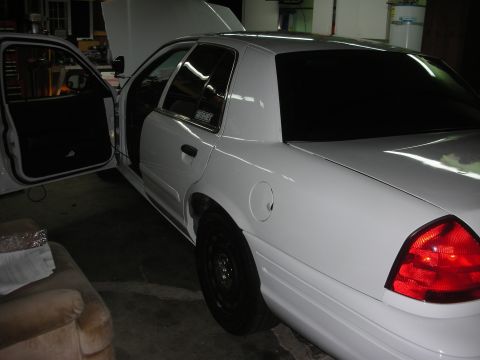 2004 Ford Crown Victoria - Three-quarter rear view of a white full-size sedan in a garage with the hood and driver's door open, showing tinted rear glass, black steel…