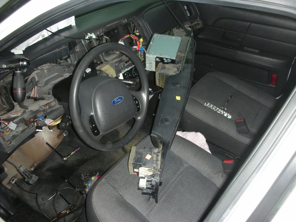 Car interior with dashboard disassembled, wires exposed, steering wheel visible