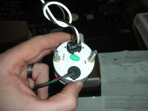 2004 Ford Crown Victoria - A hand holds a white gauge with wiring and a green 'Passed' sticker, with installation instructions in the background.