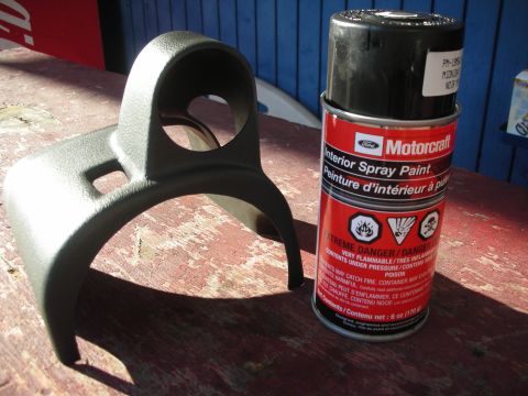 2004 Ford Crown Victoria - A black plastic gauge pod sits next to a can of Motorcraft interior spray paint on a weathered wooden table.